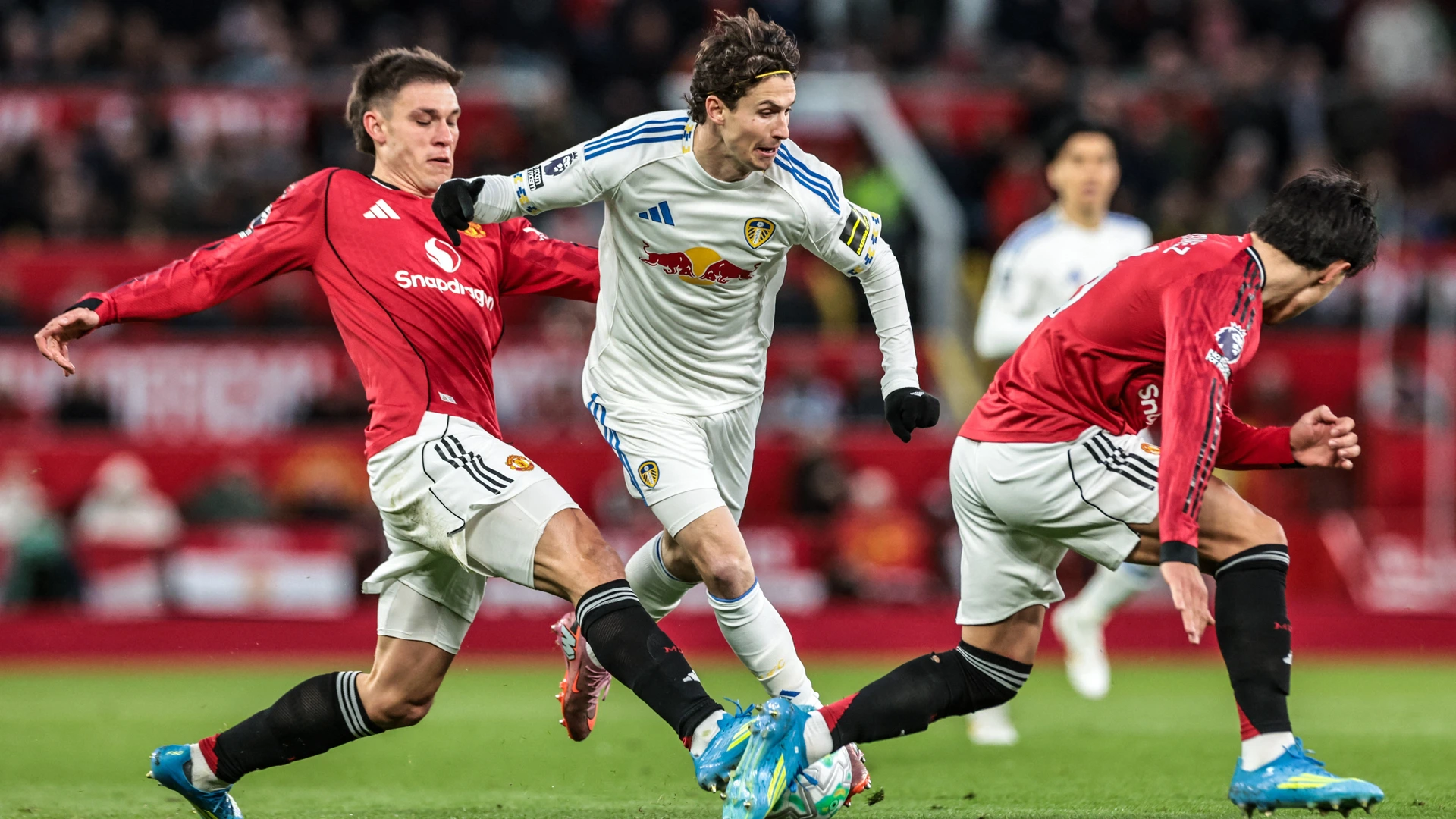 Brenden Aaronson of Leeds United is tackled by Manuel Ugarte and Lisandro Martinez of Manchester United during the Premier League match between Manchester United and Leeds United at Old Trafford, Manchester, United Kingdom, on April 13, 2026.
